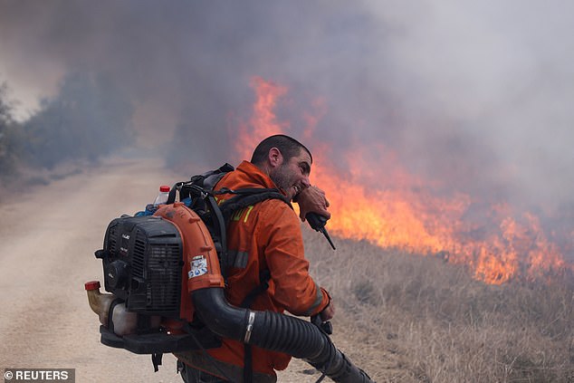 A firefighter covers his face as he attempts to extinguish flames following a rocket attack from Lebanon in the Israeli-occupied Golan Heights September 20, 2024