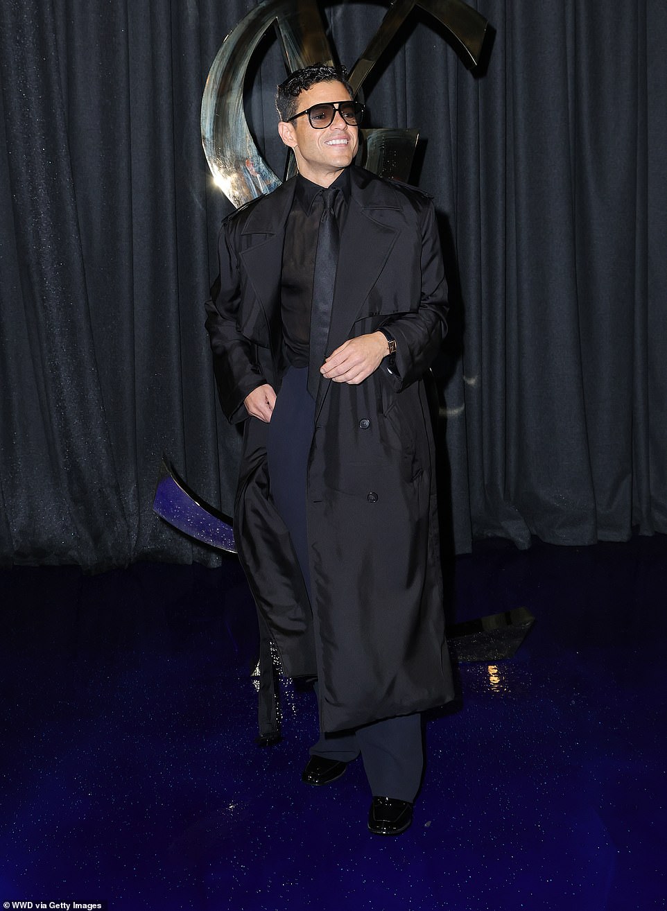 Rami Malek looked stylish in a trench coat with a black shirt and navy trousers