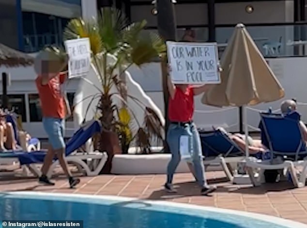 Protesters walk by the pool holding placards