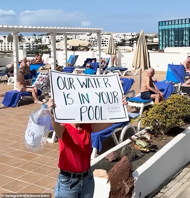 Protester holds a placard that reads 'Our Water Is In Your Pool' at the Papagayo Arena hotel during a demonstration against the hotel's alleged violation of land use regulations, as the island is hit with severe water shortages