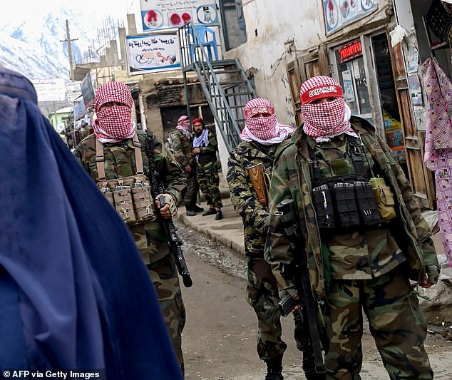 The alleged massacre comes after a crackdown by the Iranian regime on migrants trying to escape the clutches of the Taliban. Pictured: Taliban security personnel stand guard as an Afghan burqa-clad woman (right) walks along a street at a market in the Baharak district of Badakhshan province on February 26, 2024