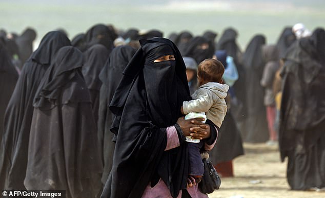 A fully veiled woman holds her baby as civilians fleeing the Islamic State's group embattled holdout of Baghouz walk in a field on February 13, 2019