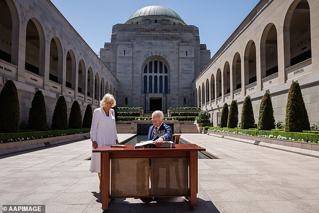 King Charles III signs another visitor's book as Queen Camilla stands next to him at the Australian War Memorial in Canberra