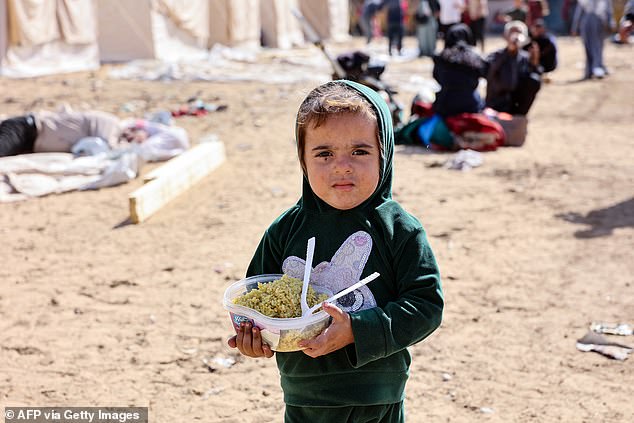 A displaced Palestinian child who fled the northern Gaza Strip carries a bowl of food in front of a newly set up tents at the Yarmouk Sports Stadium in Gaza City on October 25