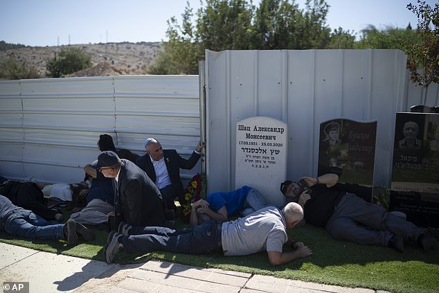 People take cover as a siren warns of incoming rockets during the funeral of Alexei Popov, who was killed during a rocket attack fired from Lebanon last weekend, at the Tel Regev cemetery in the outskirts of Haifa, northern Israel, Monday, Oct. 21, 2024