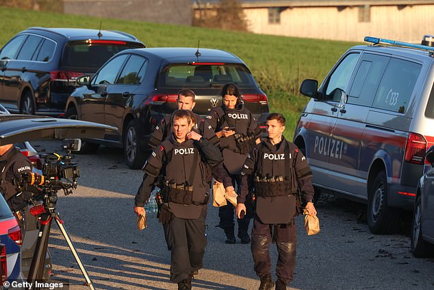 Law enforcement officers pass by media gathered during manhunt on October 28, 2024 near Rohrbach, Austria