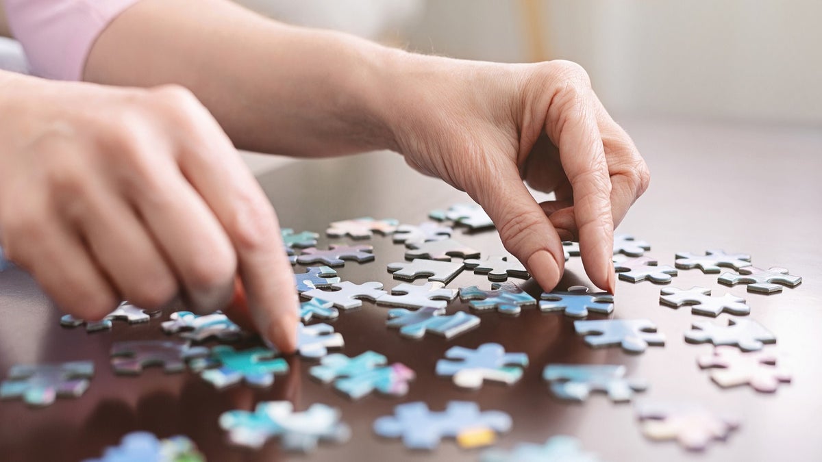 Dementia prevention. Elderly woman hands doing jigsaw puzzle at home, panorama, close up