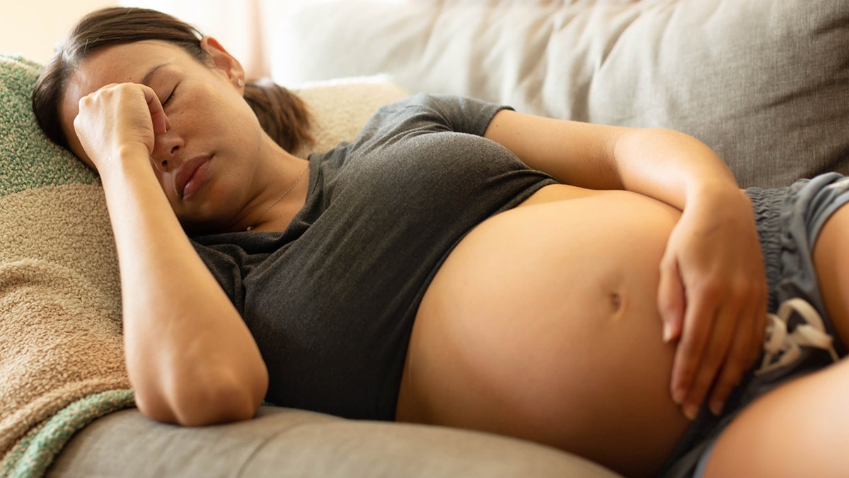 pregnant mother trying to rest at home, lying on her couch holding her head.