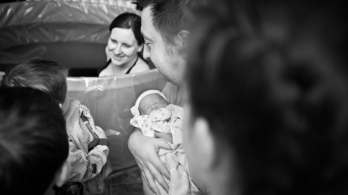 father showing his newborn son to his other children as their mother looks on