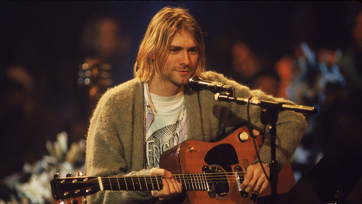 Kurt Cobain sitting on stage in front of a microphone with a guitar