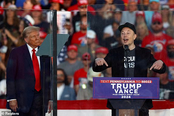 FILE PHOTO: Tesla CEO and X owner Elon Musk speaks as Republican presidential nominee and former U.S. president Donald Trump looks on during a rally at the site of the July assassination attempt against Trump, in Butler, Pennsylvania, U.S., October 5, 2024. REUTERS/Carlos Barria/File Photo