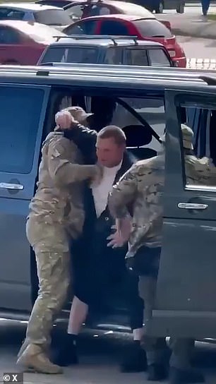 A Ukrainian men is pictured above as he is dragged into a vehicle by military recruitment officers