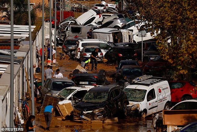 People clean up a mud-covered street next to piled up cars after heavy rains in Alfafar, in Valencia, Spain, November