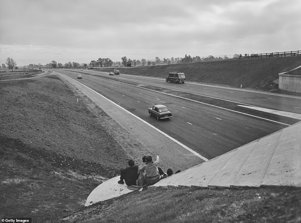 A group of children sit on the verge watching traffic pass on the M1. When it opened, there was no speed limit. That wasn't introduced until 1967