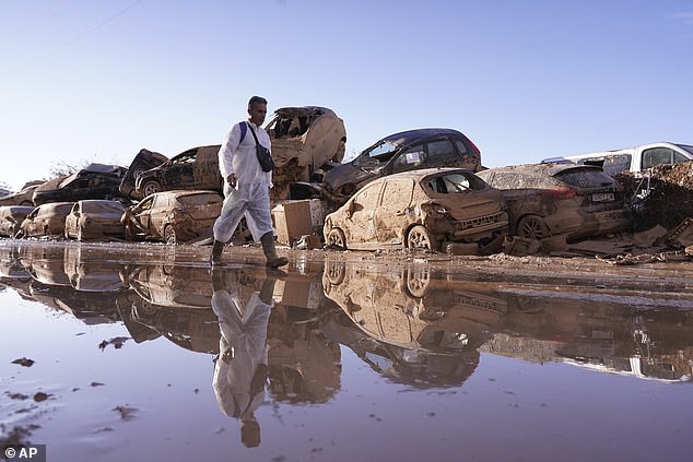 A man walks past stacked up cars after floods in Catarroja that left hundreds dead or missing in the Valencia region in Spain, Tuesday, Nov. 12, 2024