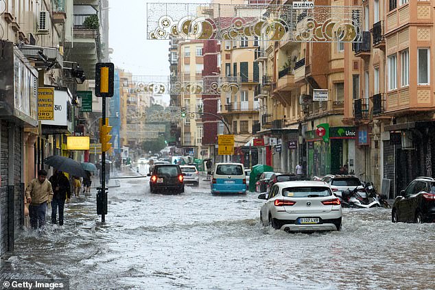 Cars and pedestrians push through floodwaters near to the El Perchel quarter of Malaga