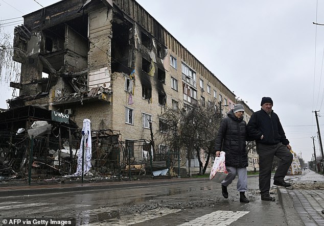 Pedestrians walk past a damaged residential building in the village of Gostomel, close to Kyiv, on April 22, 2022