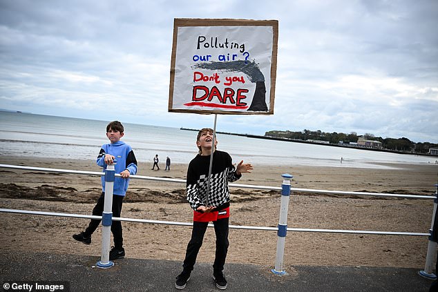 Two young boys on Weymouth seafront hold up a sign saying 'Polluting the air? Don't you dare'