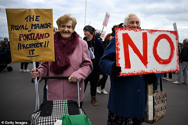 Two ladies hold up signs, one says 'The Royal manor of Portland. Respect It!' and the other is 'NO' written in large red letters