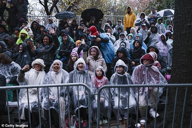 Parade goers wear ponchos and hold umbrellas