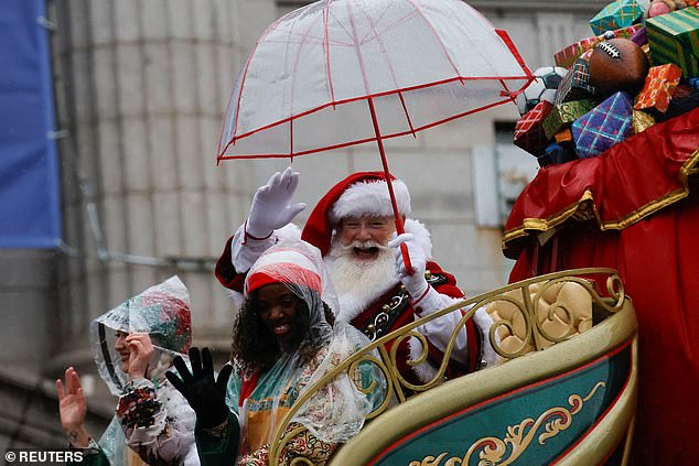 Santa Claus waves to parade goers while holding an umbrella