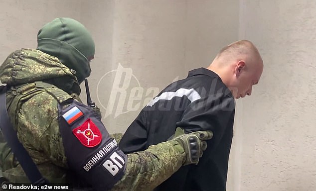 James Scott Rhys Anderson, 22, was seen bent double by an armed guard as he was hauled from his detention cell to face interrogation by the autocrat's propagandists