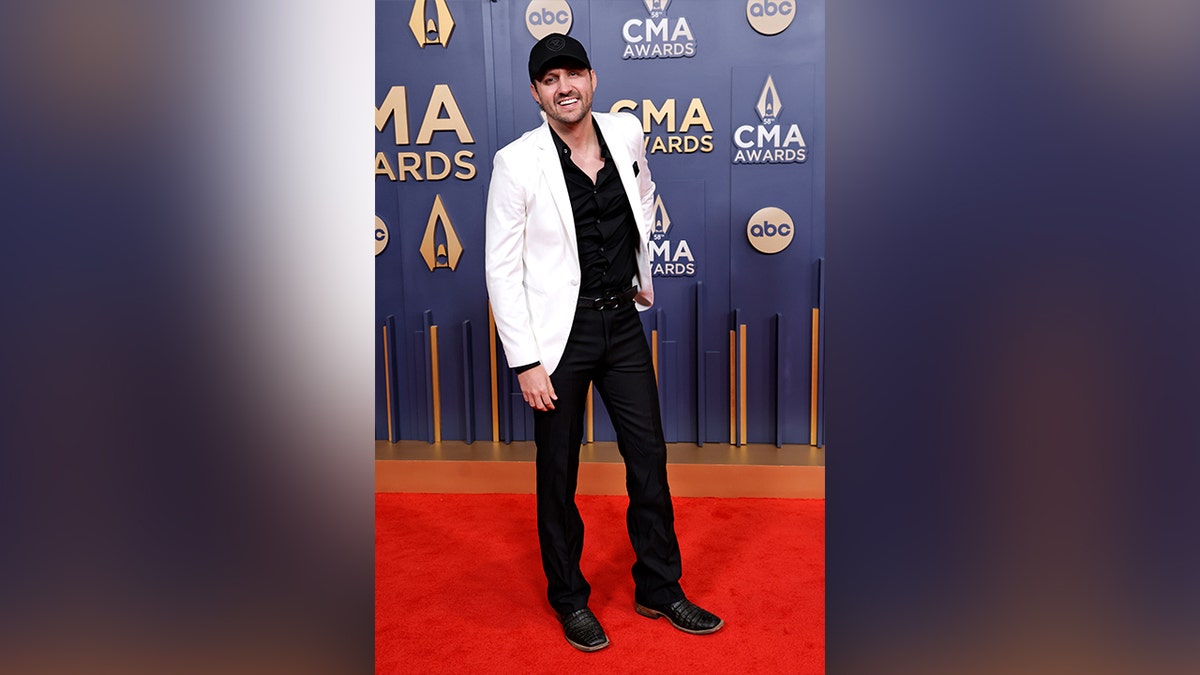 Drew Baldridge paired his white suit jacket and black pants with a black baseball cap on the 2024 CMA Awards red carpet.