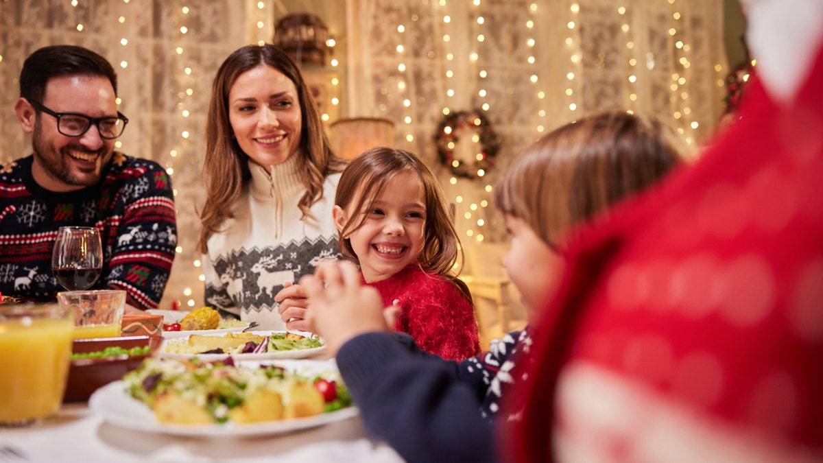 Happy parents and their kids talking while having dinner at dining table.