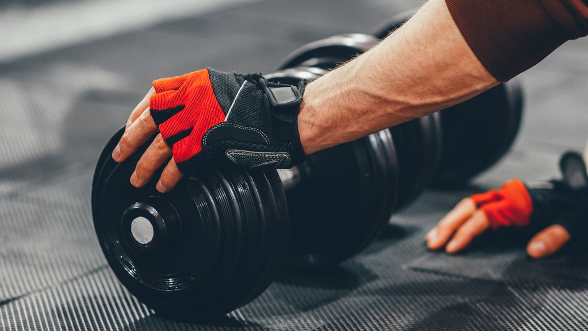 Man about to pick up dumbbell with workout gloves on