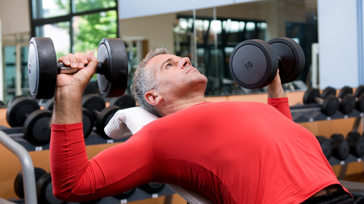 Mature man lifting dumbells at fitness gym