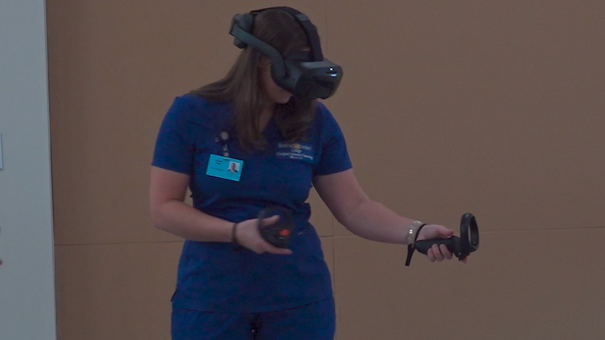 A nursing student wearing virtual reality goggles and holding controllers, engaging in a clinical training simulation.