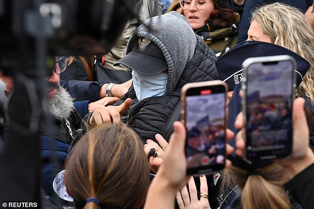 A man hiding his face is surrounded by French police, journalists and protesters as he leaves after the verdict in the trial for Dominique Pelicot