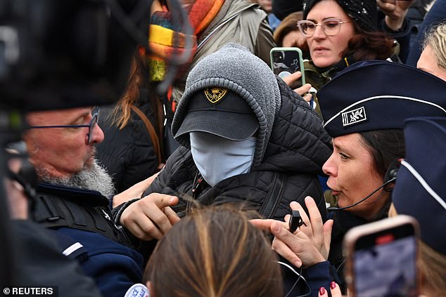 A man hiding his face is surrounded by French police, journalists and protesters as he leaves after the verdict in the trial for Dominique Pelicot