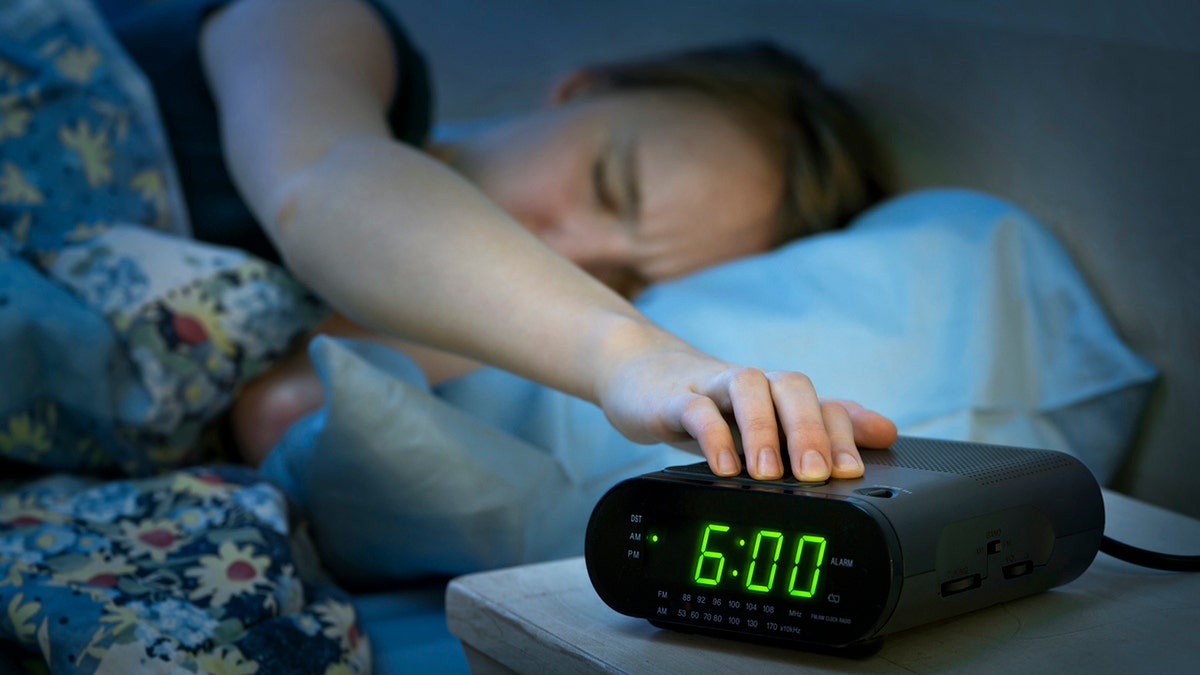 Young woman pressing snooze button on early morning digital alarm clock