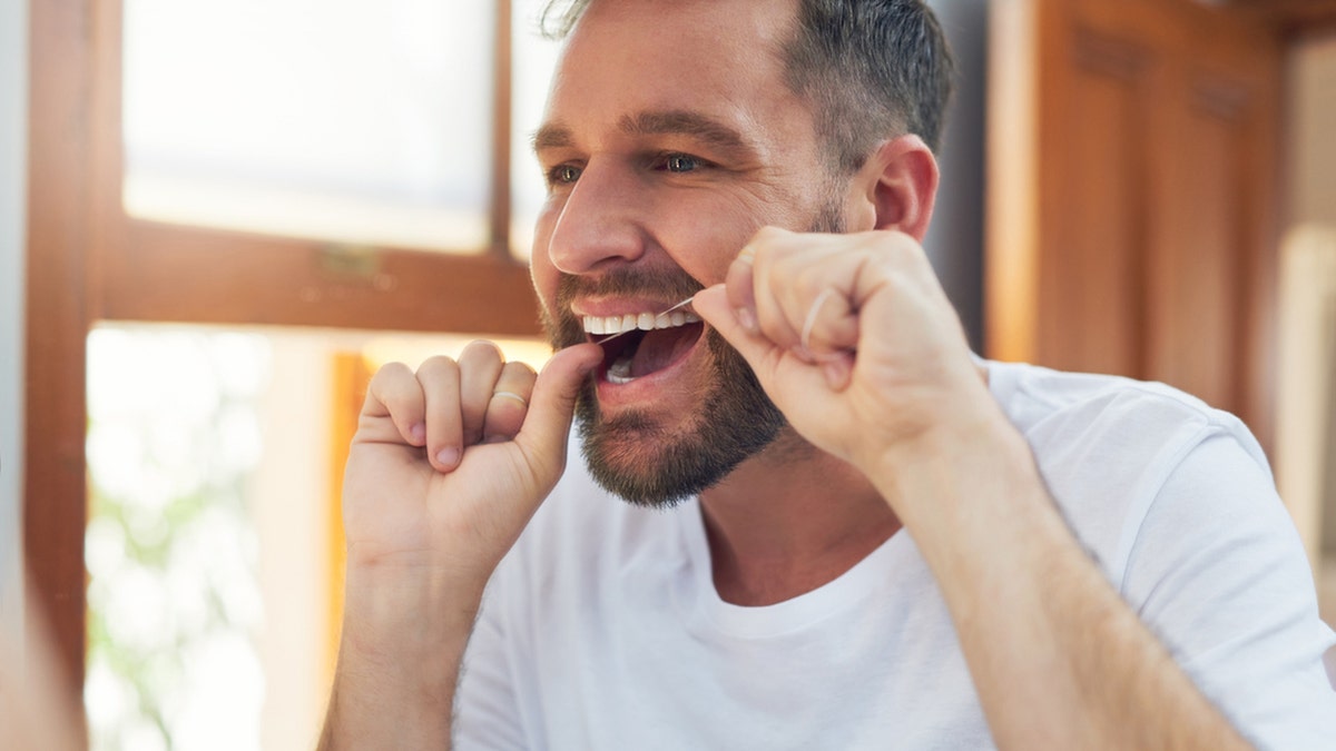 man flossing his teeth in the bathroom