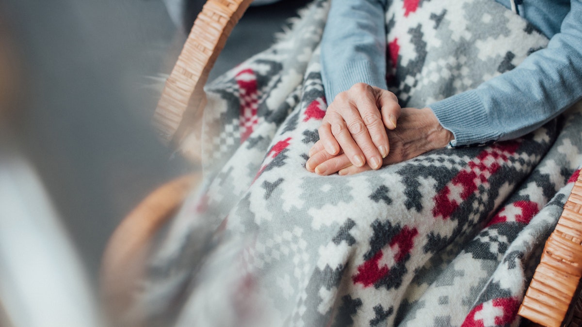 woman sitting in wicker rocking chair with blanket and folded hands at home