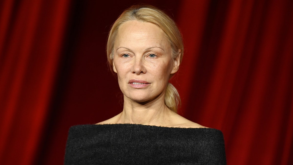 Pamela Anderson in a black gown looks serious on the carpet wearing no makeup