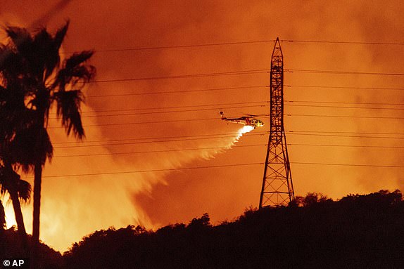 A helicopter drops water on the Palisades Fire in Mandeville Canyon, Friday, Jan. 10, 2025, in Los Angeles. (AP Photo/Ethan Swope)