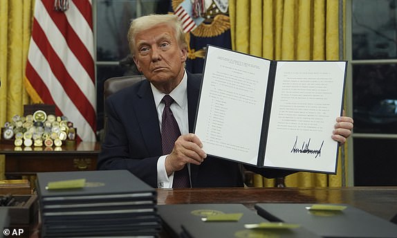 President Donald Trump holds up an executive order commuting sentences for people convicted of Jan. 6 offenses in the Oval Office of the White House, Monday, Jan. 20, 2025, in Washington. (AP Photo/Evan Vucci)