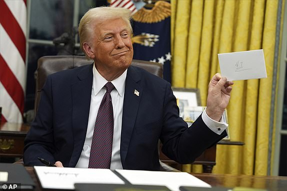 President Donald Trump holds up the letter that former President Joe Biden left for him in the desk as he signs executive orders in the Oval Office of the White House, Monday, Jan. 20, 2025, in Washington. (AP Photo/Evan Vucci)