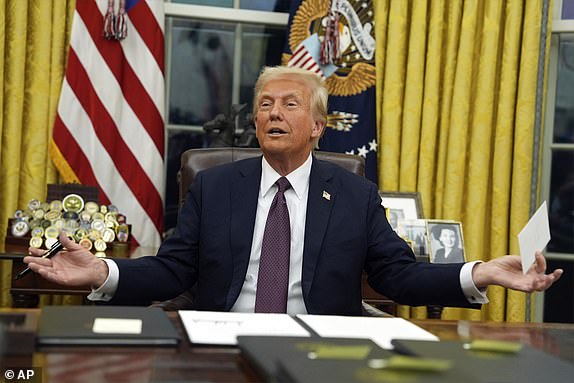 President Donald Trump holds up the letter that former President Joe Biden left for him in the desk as he signs executive orders in the Oval Office of the White House, Monday, Jan. 20, 2025, in Washington. (AP Photo/Evan Vucci)