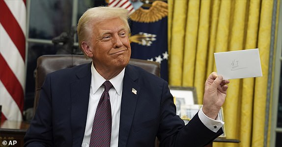 President Donald Trump holds up the letter that former President Joe Biden left for him in the desk as he signs executive orders in the Oval Office of the White House, Monday, Jan. 20, 2025, in Washington. (AP Photo/Evan Vucci)