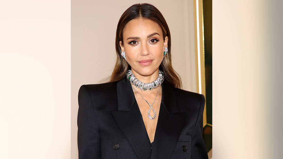 Jessica Alba in a black blazer and large choker necklace poses on the carpet