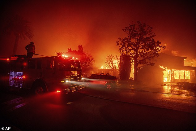 Fire crews battle the blaze as it burns structures in the Pacific Palisades area yesterday