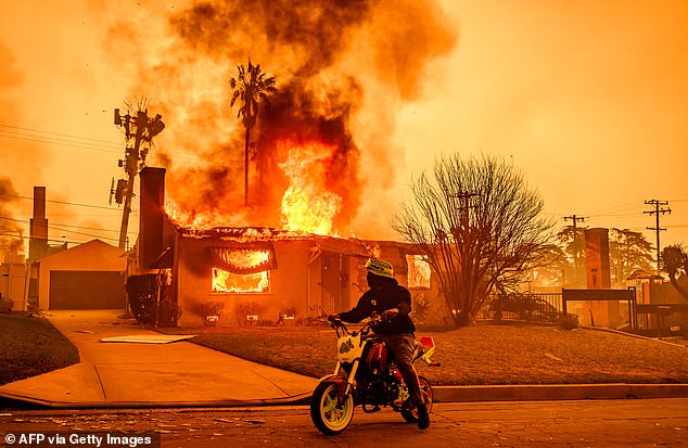 A motorcyclist stops to look at a burning home during the Eaton fire