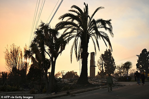 Residents are pictured walking past a burned home after looking for belongings at their home during the Palisades Fire in Pacific Palisades on Thursday