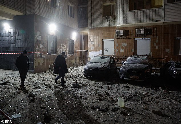 Local people walk near damaged cars at the site of drone debris falling on a residential building, in Kyiv, Ukraine, January 10, 2025