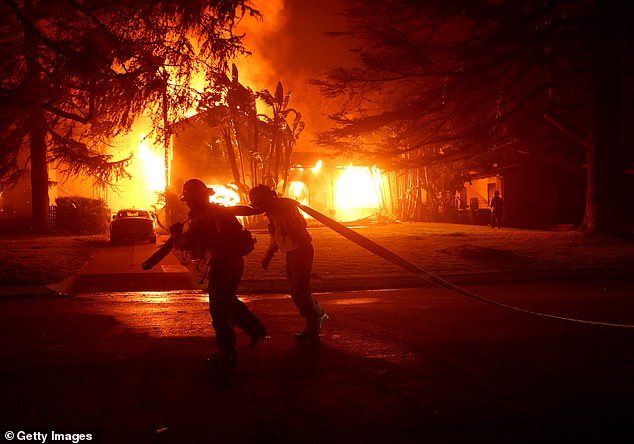 Firefighters pull a hose in front of a burning home in Altadena as the Eaton Fire moved through the area on Wednesday