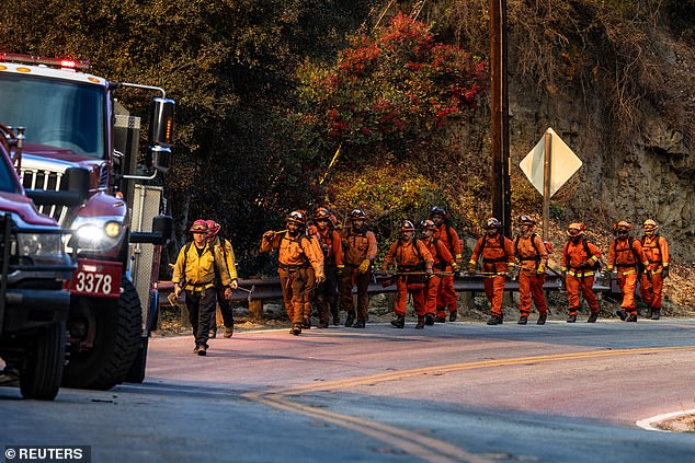 A team of firefighters walk near the Palisades Fire in Malibu - one of six simultaneous blazes engulfing Los Angeles