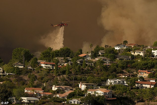 A helicopter drops water on homes affected by the Palisades Fire in Mandeville Canyon